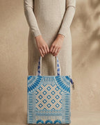 Model holding a blue and beige patterned tote bag against a beige background