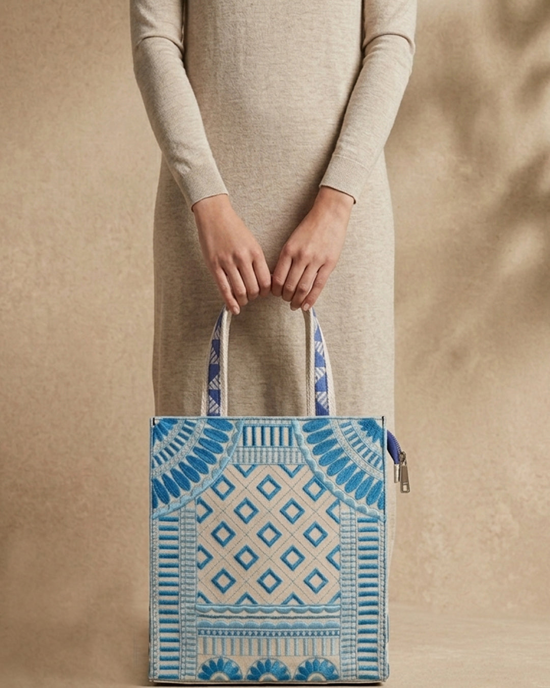 Model holding a blue and beige patterned tote bag against a beige background