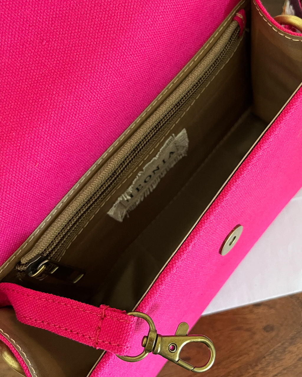 Close-up inside view of a fuchsia  pink crossbody sling women's bag with a zipper and clasp for keys.