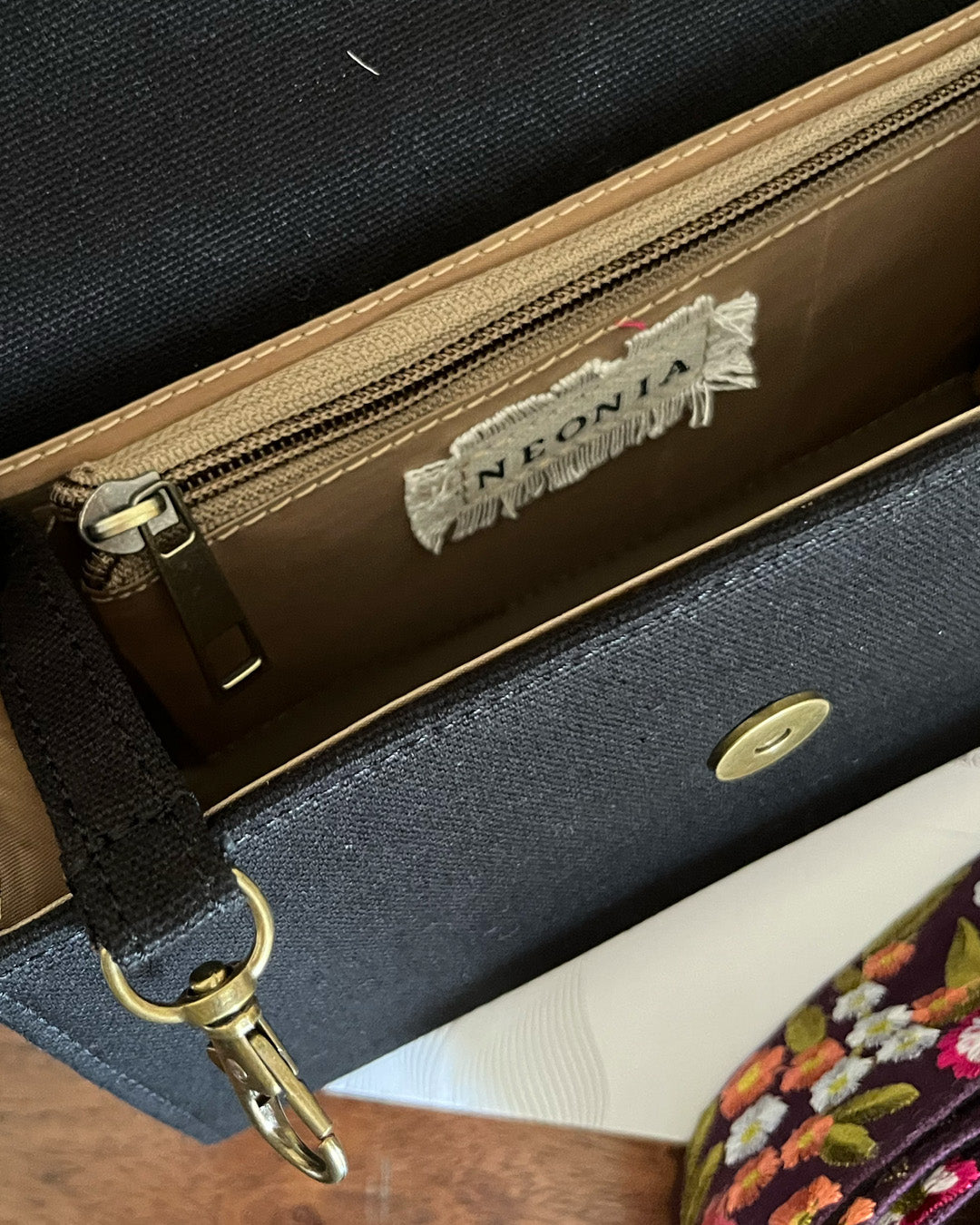 Inside of a black sling crossbody bag with inside zipper and clasp for keys , featuring a visible brand label -Neonia.